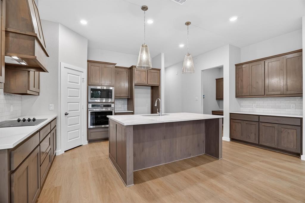 321 Skeen Peak Springtown, TX 76082 - Photo 7 of 37 Kitchen featuring wood-finish flooring, an oversized island with a built-in sink, pendant lighting, stainless steel appliances, and extensive cabinetry