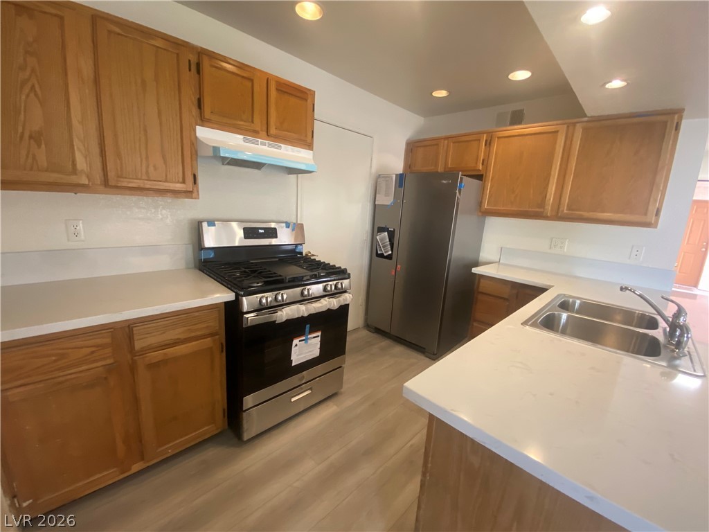 7570 West Flamingo Road, Unit 125 Las Vegas, NV 89147 - Photo 3 of 29 Kitchen featuring stainless steel appliances, recessed lighting, brown cabinets, under cabinet range hood, and light wood-style flooring