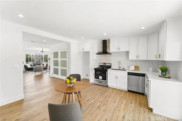 a kitchen with stainless steel appliances a stove a sink a refrigerator white cabinets and wooden floor