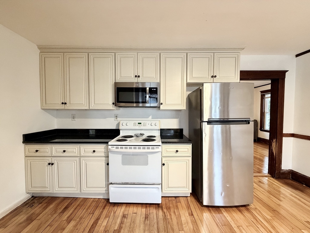 20 Clark Street, Unit 1 Framingham, MA 01702 - Photo 16 of 17 a kitchen with a refrigerator a stove and white cabinets with wooden floor