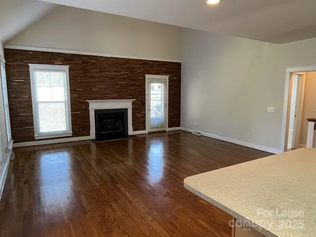 an empty room with wooden floor fireplace and windows