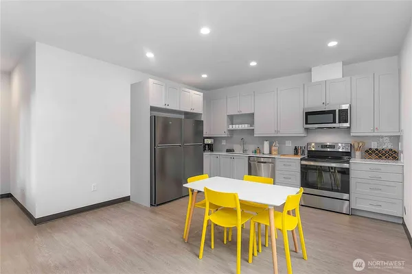 a kitchen with stainless steel appliances granite countertop a dining table chairs refrigerator and sink