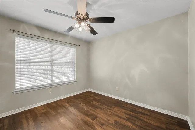 an empty room with wooden floor chandelier fan and windows
