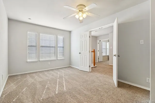 an empty room with chandelier fan and windows