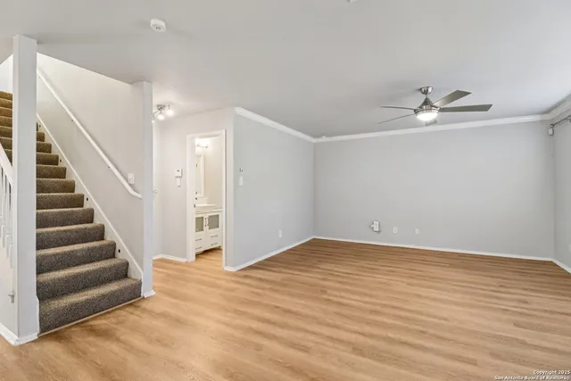 a view of an empty room with wooden floor and a ceiling fan