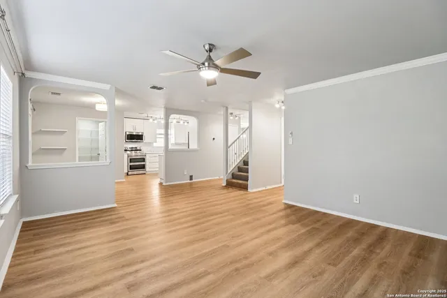 an empty room with wooden floor a ceiling fan and kitchen view