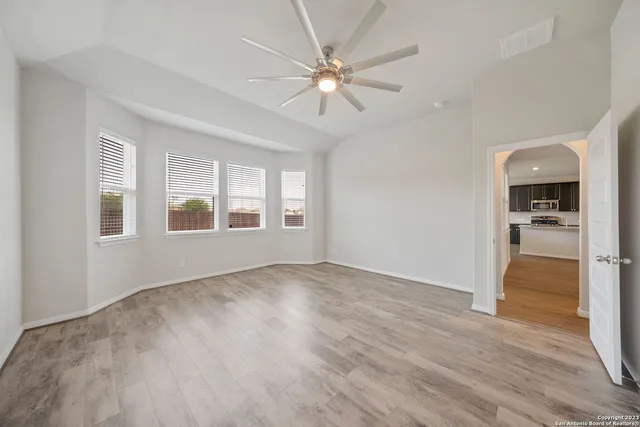 an empty room with wooden floor chandelier fan and windows