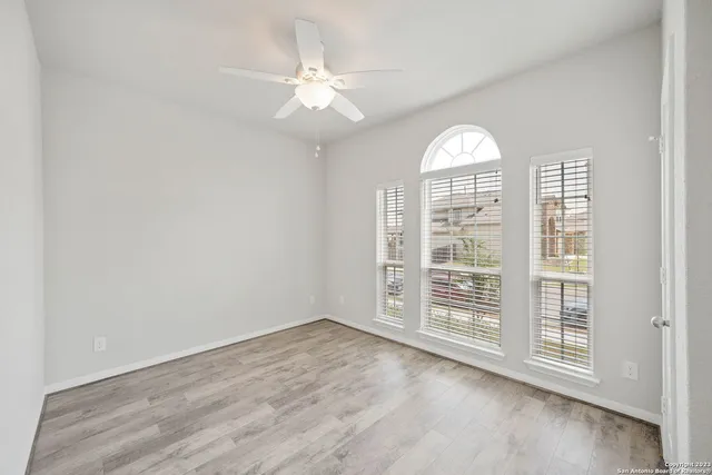 an empty room with wooden floor fan and windows