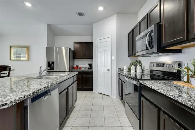 a kitchen with stainless steel appliances granite countertop a refrigerator a stove a sink a microwave and a dining table with wooden cabinet