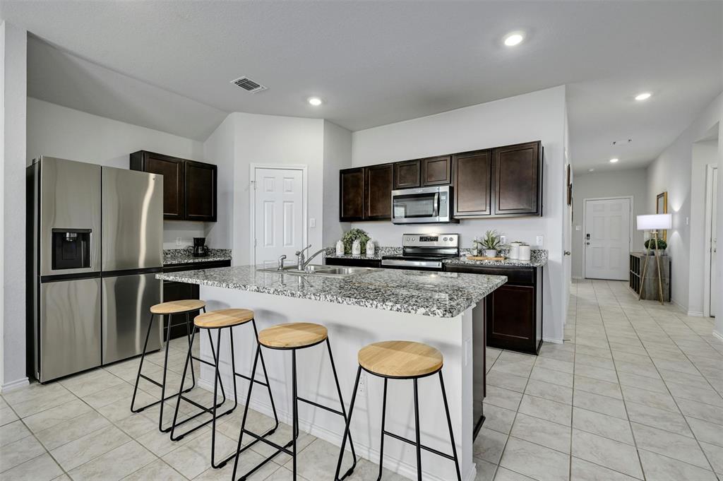 1045 Taggart Trail Jarrell, TX 76537 - Photo 5 of 19 Kitchen featuring dark brown cabinetry, stainless steel appliances, light stone countertops, a kitchen breakfast bar, and recessed lighting
