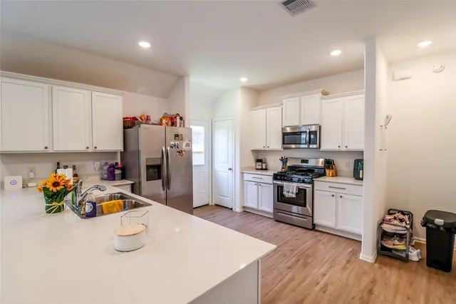 a kitchen with a sink dishwasher a stove and white cabinets with wooden floor
