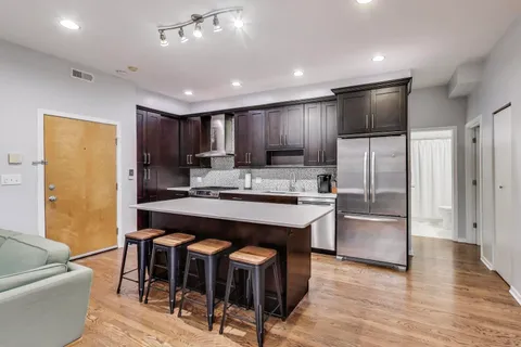 a kitchen with stainless steel appliances kitchen island granite countertop a refrigerator a stove a sink a dining table and chairs with wooden floor