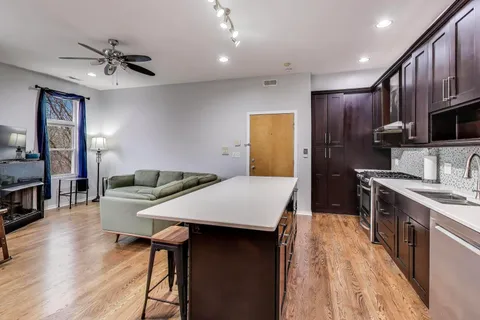 a kitchen with stainless steel appliances kitchen island granite countertop a refrigerator a stove top oven a sink dishwasher and wooden cabinets with wooden floor