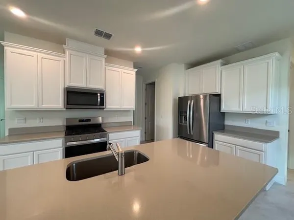 a kitchen with granite countertop a refrigerator a sink a stove a microwave and cabinets