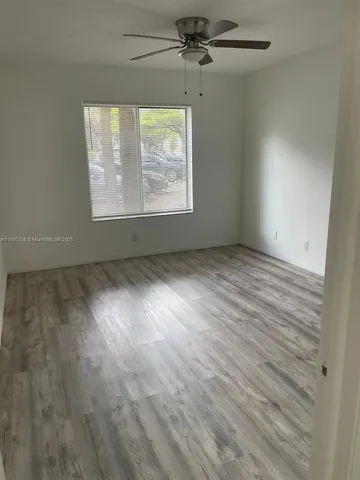 an empty room with wooden floor chandelier fan and windows
