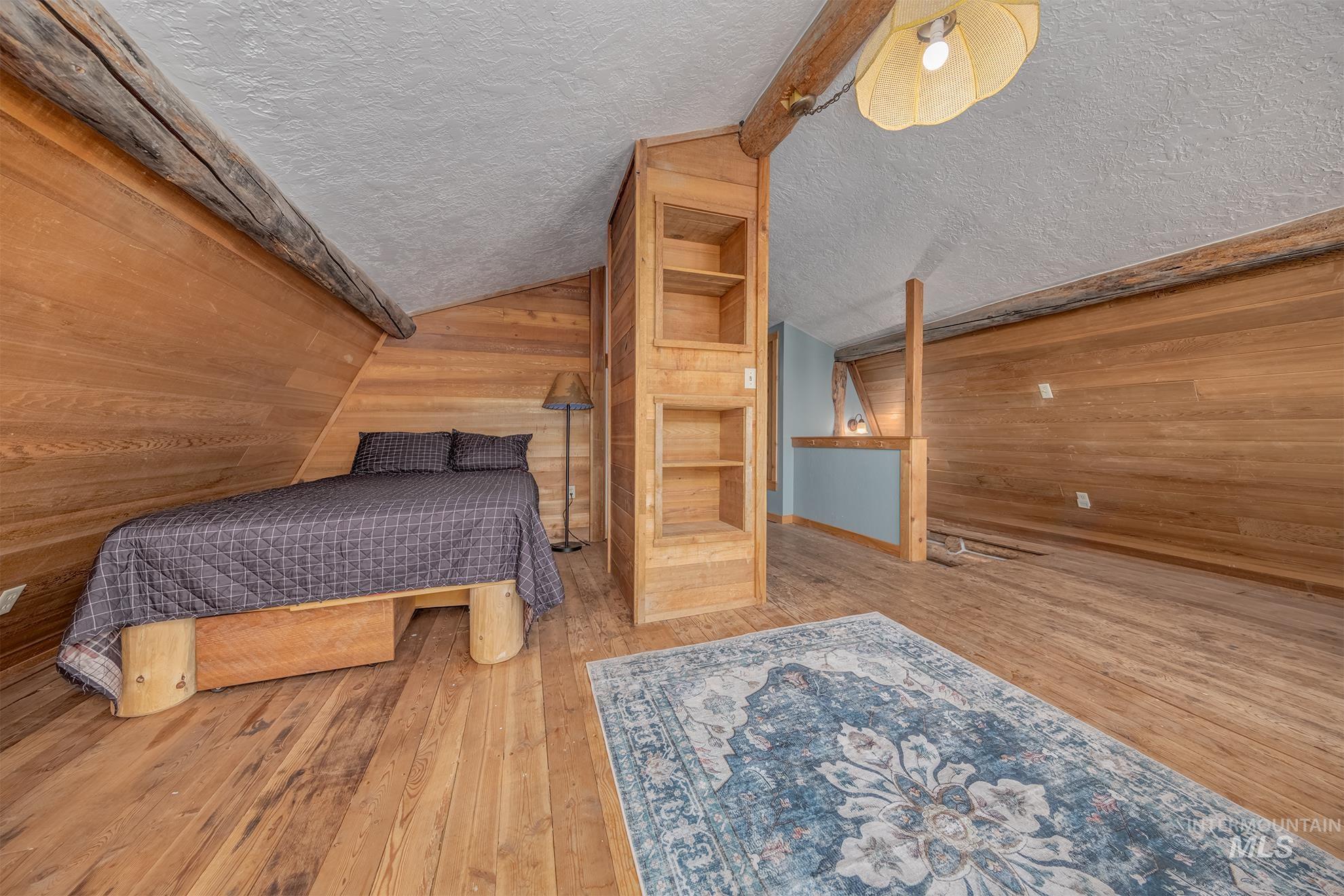2150 Seid Creek Road Cambridge, ID 83610 - Photo 23 of 50 Wood-paneled room featuring wood-finish flooring, exposed ceiling beams, a built-in shelving unit, and a textured ceiling