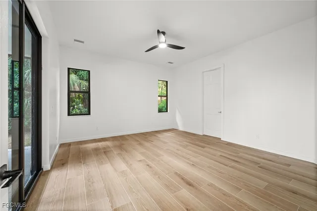 an empty room with wooden floor ceiling fan and windows