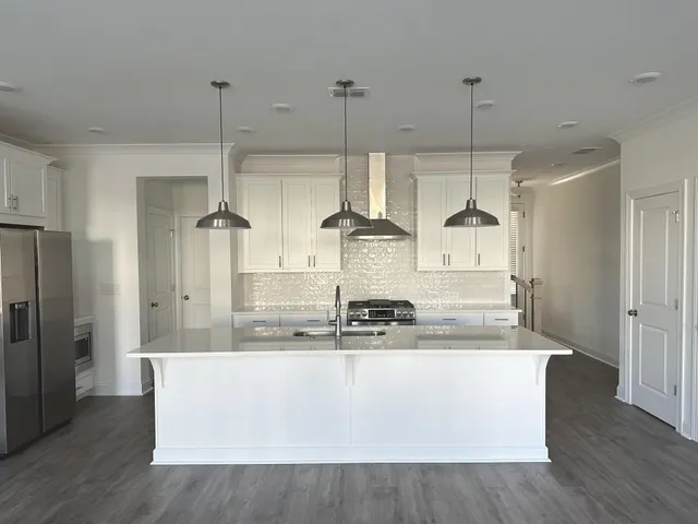 a kitchen with kitchen island stainless steel appliances granite countertop a sink a refrigerator and a wooden floor