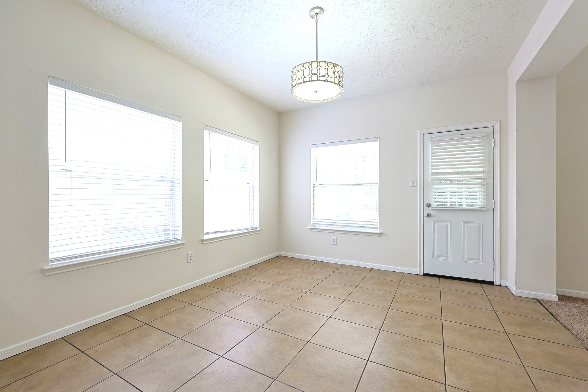 23019 Eastgate Village Drive Spring, TX 77373 - Photo 12 of 46 Bright and inviting room with large windows, neutral walls, and tile flooring. Features a modern light fixture and a door leading outside, perfect for flexible use as a dining or sitting area.