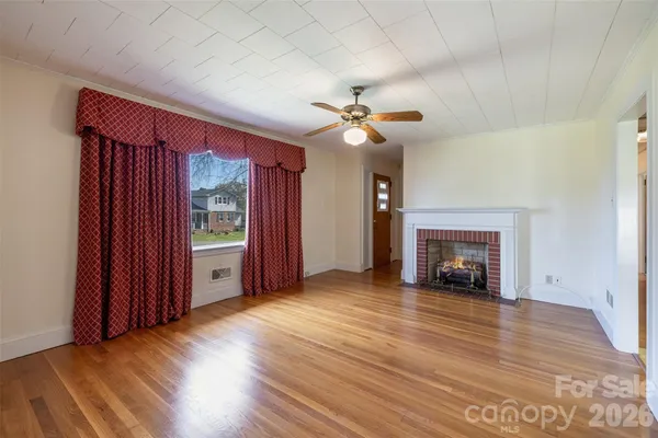 an empty room with wooden floor fireplace and windows