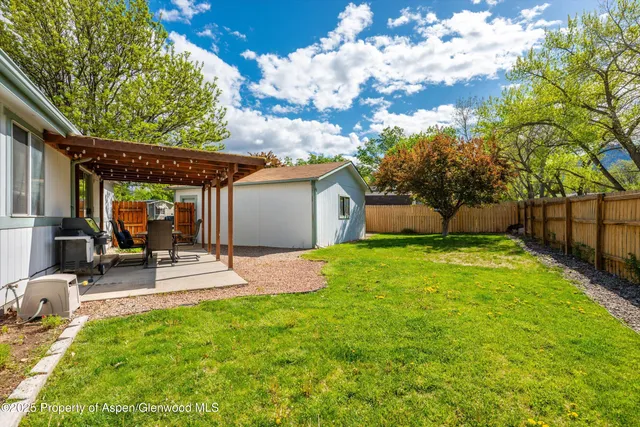 a view of a backyard with table and chairs potted plants and a large tree