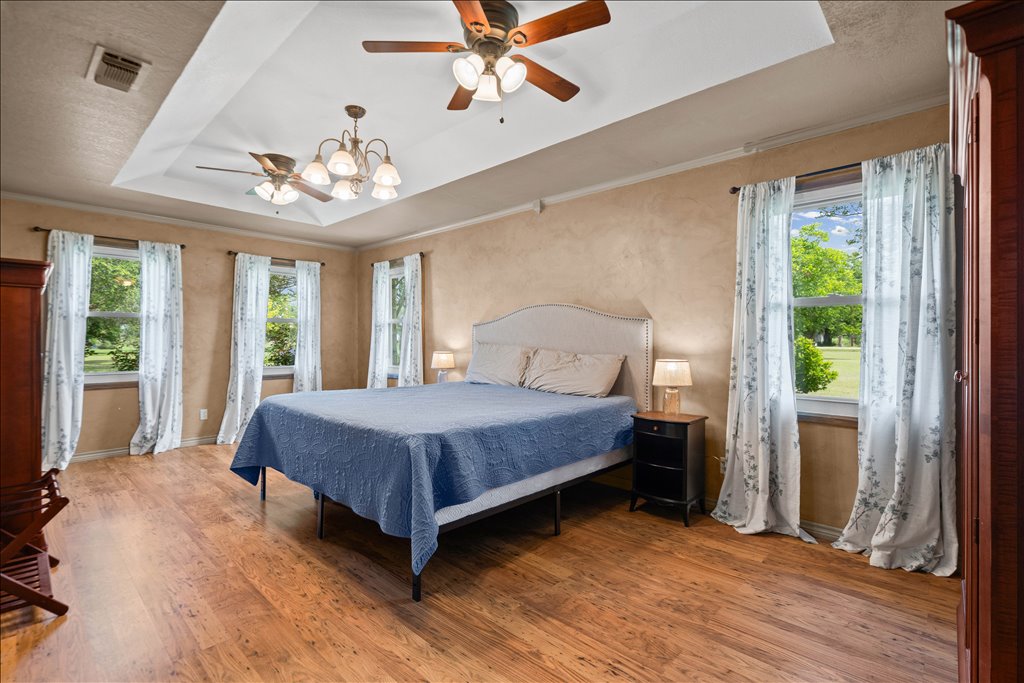 2421 Post Oak Road Webberville, TX 78653 - Photo 14 of 36 Welcome to the primary suite, and wow, this room is huge! You’ve got more of those beautiful wood floors, a gorgeous tray ceiling with double ceiling fans, and multiple windows that let the country views right in.