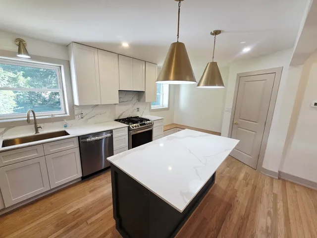 a kitchen with stainless steel appliances a stove a sink a window and wooden floor