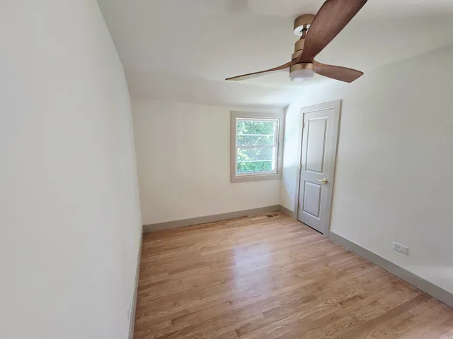 an empty room with wooden floor chandelier fan and windows