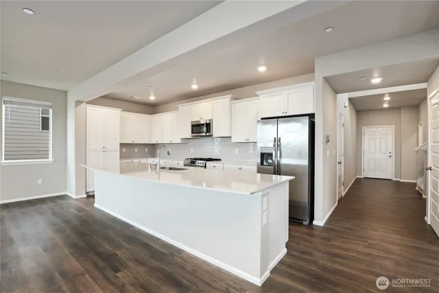 a large white kitchen with stainless steel appliances lots of counter top space and wooden floor