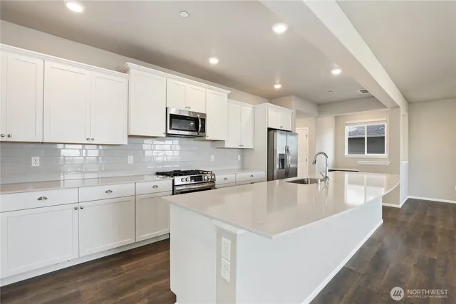 a large kitchen with stainless steel appliances granite countertop a stove a sink a refrigerator and white cabinets with wooden floor