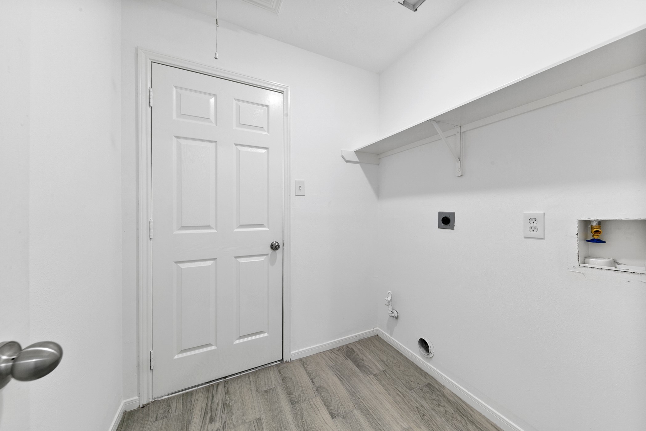 12014 Raven View Drive Houston, TX 77067 - Photo 12 of 29 This is a compact utility room with hookups for a washer and dryer. It features a white door, light-colored walls, hardwood flooring, and a shelf for storage.