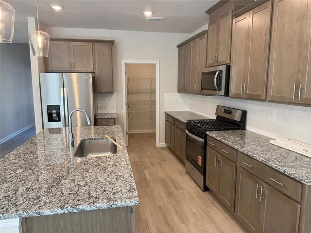 a kitchen with stainless steel appliances granite countertop a refrigerator a stove and a sink with wooden floors