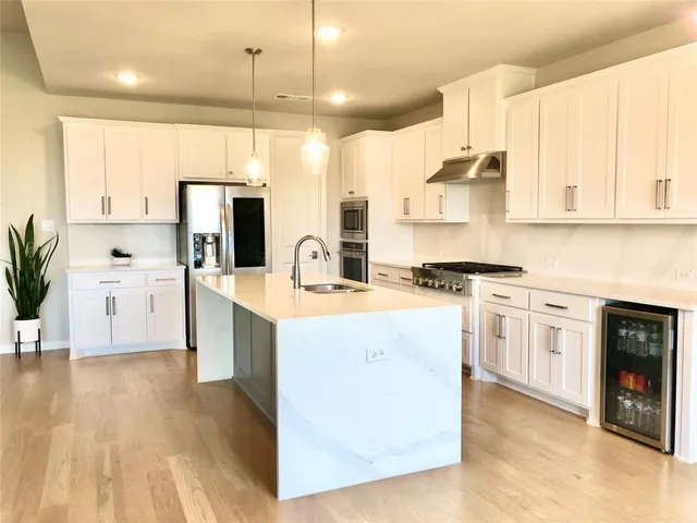 a kitchen with kitchen island a stove a sink a refrigerator and white cabinets with wooden floor