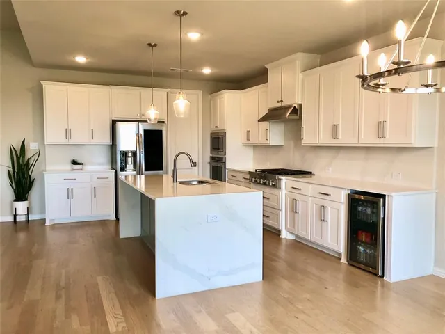 a kitchen with stainless steel appliances a stove top oven a sink a refrigerator and white cabinets with wooden floor