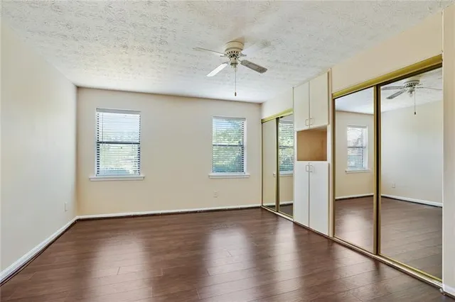 an empty room with wooden floor a ceiling fan and windows
