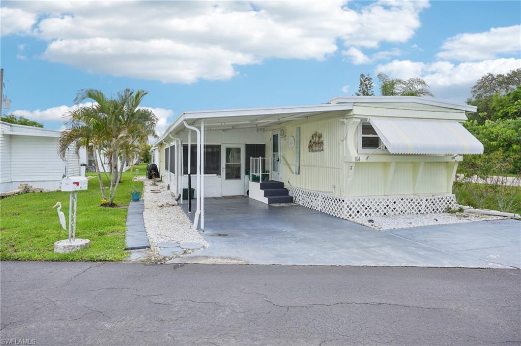 104 Willow Lane, Unit 30 Naples, FL 34114 - Photo 3 of 30 Mobile home featuring entry steps, a front lawn, an attached carport, a sunroom, and driveway