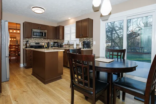 a kitchen with stainless steel appliances granite countertop a stove a refrigerator a microwave a dining table and chairs with wooden floor