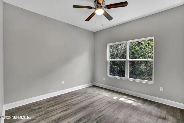 an empty room with wooden floor windows and fan