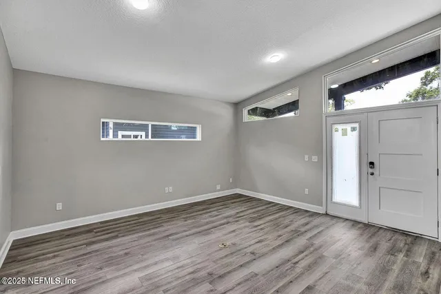 a view of an empty room with wooden floor and a window
