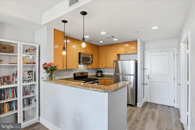 a kitchen with stainless steel appliances granite countertop a refrigerator a oven a sink and a dining table with wooden floor