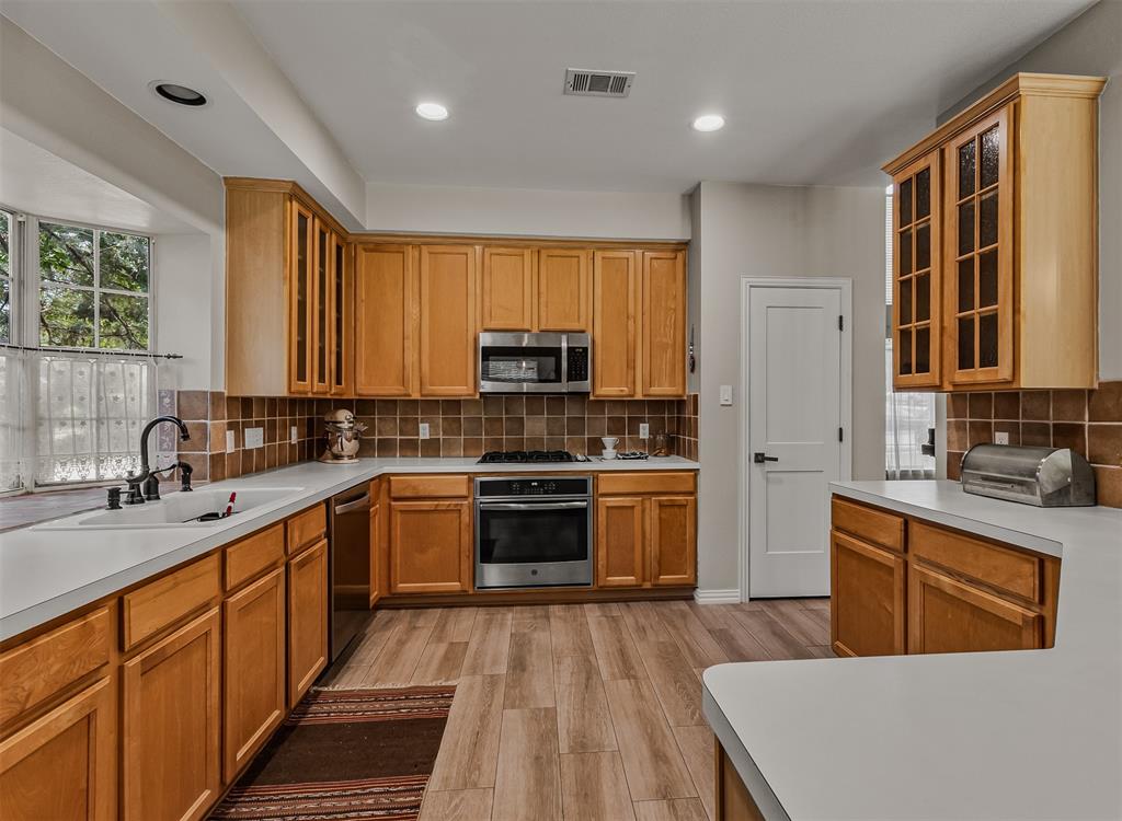 9301 Nottingham Court Rowlett, TX 75088 - Photo 7 of 39 Kitchen featuring wood cabinetry, white countertops, stainless steel appliances, a tile backsplash, and wood-finish flooring