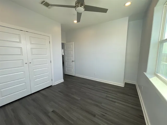 an empty room with wooden floor closet and windows