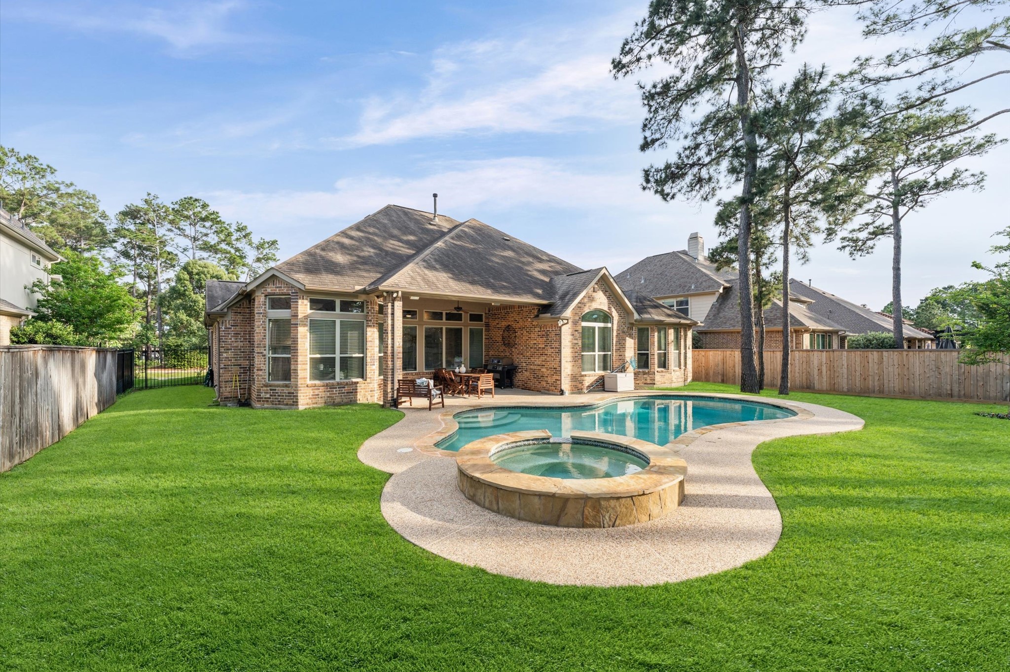 70 Valera Ridge Drive Spring, TX 77389 - Photo 5 of 37 This photo showcases a spacious backyard featuring a well-maintained lawn, a stylish brick house, and a beautiful pool with a hot tub. The area is surrounded by a wooden fence and tall trees, providing privacy and a serene atmosphere.