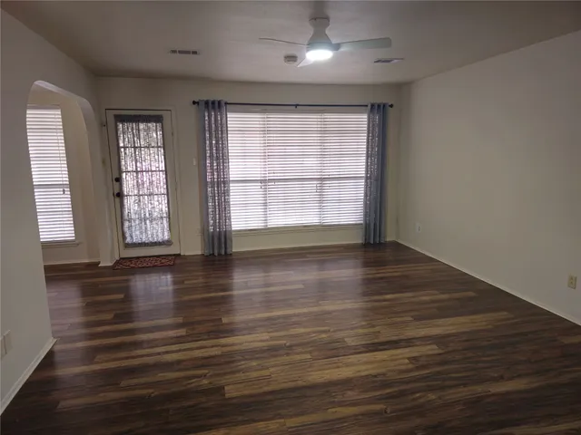 an empty room with wooden floor and windows with curtains