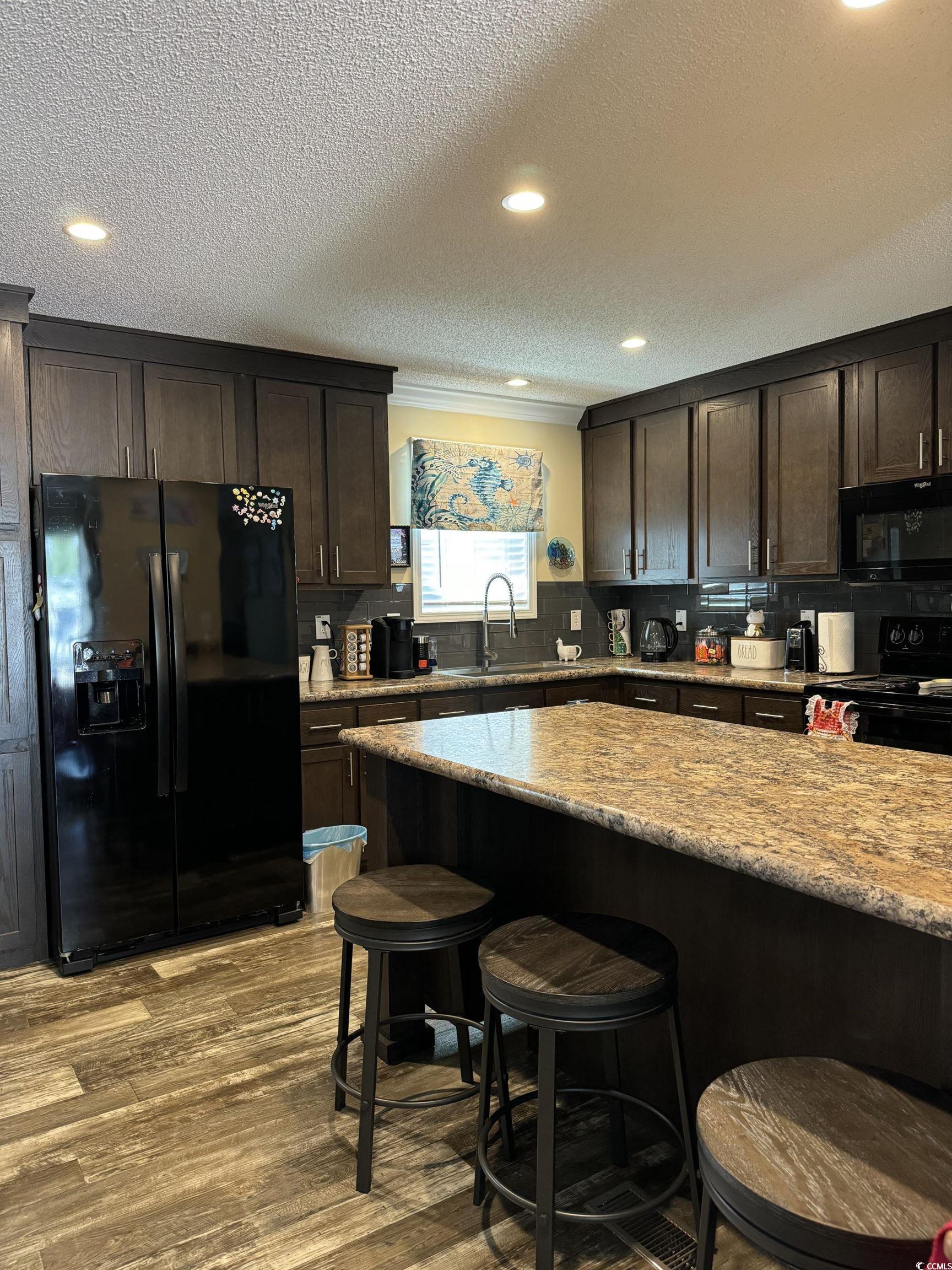 1651 Perry Circle Myrtle Beach, SC 29577 - Photo 13 of 32 Kitchen featuring dark brown cabinetry, black appliances, a breakfast bar, recessed lighting, and light stone counters