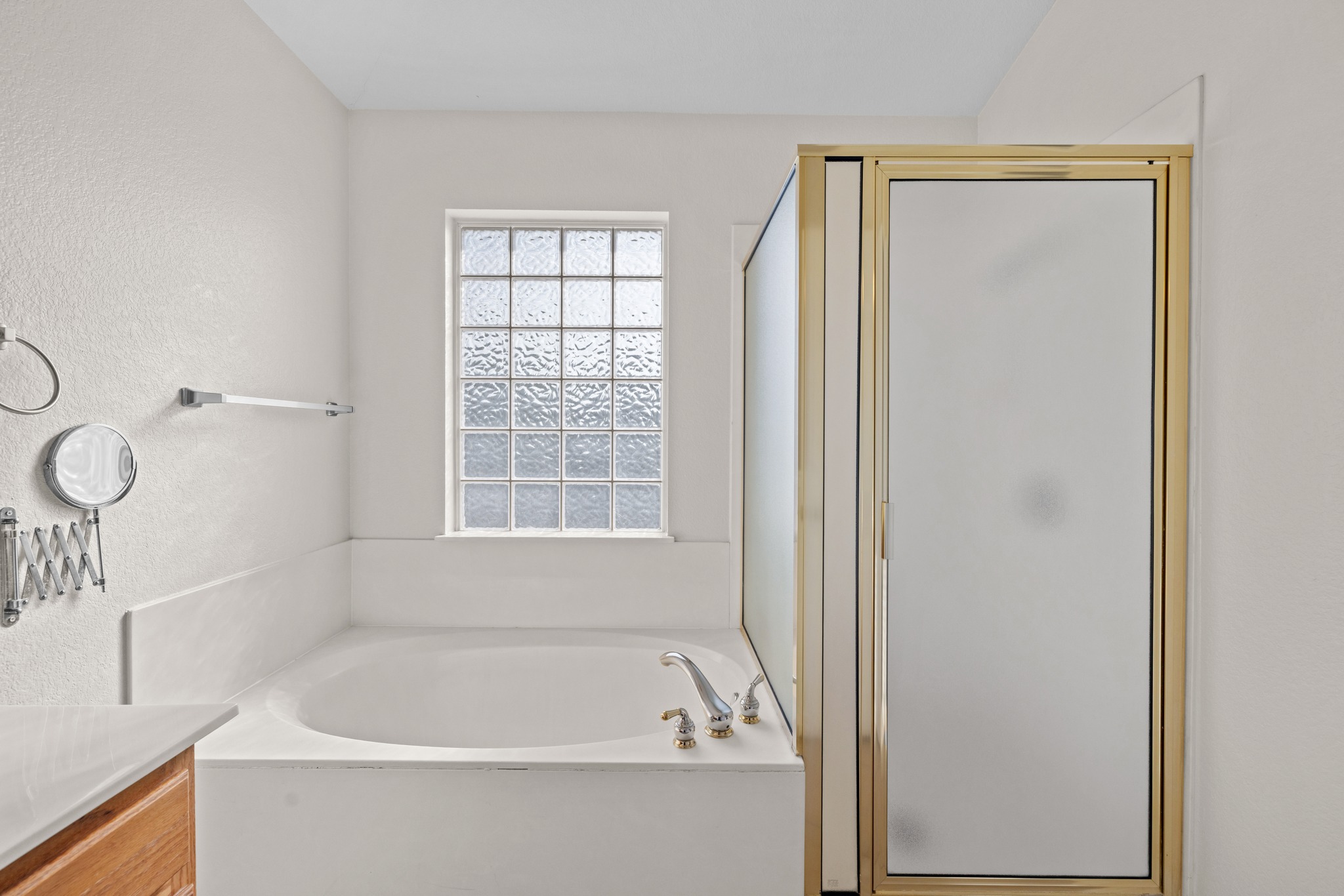 3410 Flowstone Lane Round Rock, TX 78681 - Photo 21 of 38 Bright bathroom featuring a soaking tub with a glass block window for natural light and privacy, alongside a separate enclosed shower with frosted glass doors.