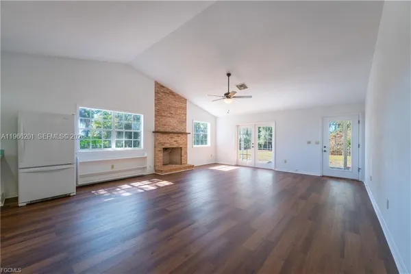 an empty room with wooden floor chandelier and windows
