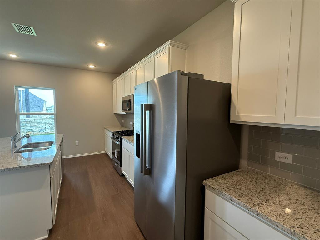 12212 Dillon Fls Drive Austin, TX 78747 - Photo 14 of 40 Kitchen with stainless steel appliances, white cabinetry, light stone countertops, dark wood finished floors, and recessed lighting
