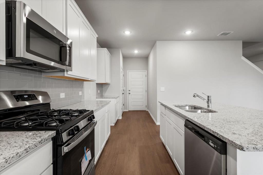 12212 Dillon Fls Drive Austin, TX 78747 - Photo 15 of 40 Kitchen featuring stainless steel appliances, light stone countertops, white cabinetry, dark wood-style flooring, and decorative backsplash
