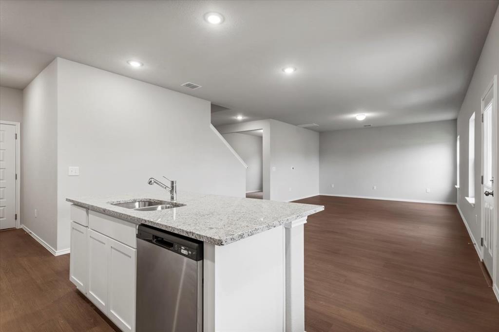 12212 Dillon Fls Drive Austin, TX 78747 - Photo 16 of 40 Kitchen with stainless steel dishwasher, white cabinets, an island with sink, light stone counters, and dark wood finished floors